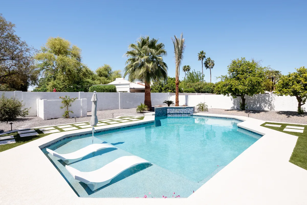 A sparkling swimming pool surrounded by palm trees and comfortable lounge chairs, with a water feature creating a resort-like ambiance. The setting is inviting for group relaxation, poolside BBQs, and informal gatherings after a productive day.