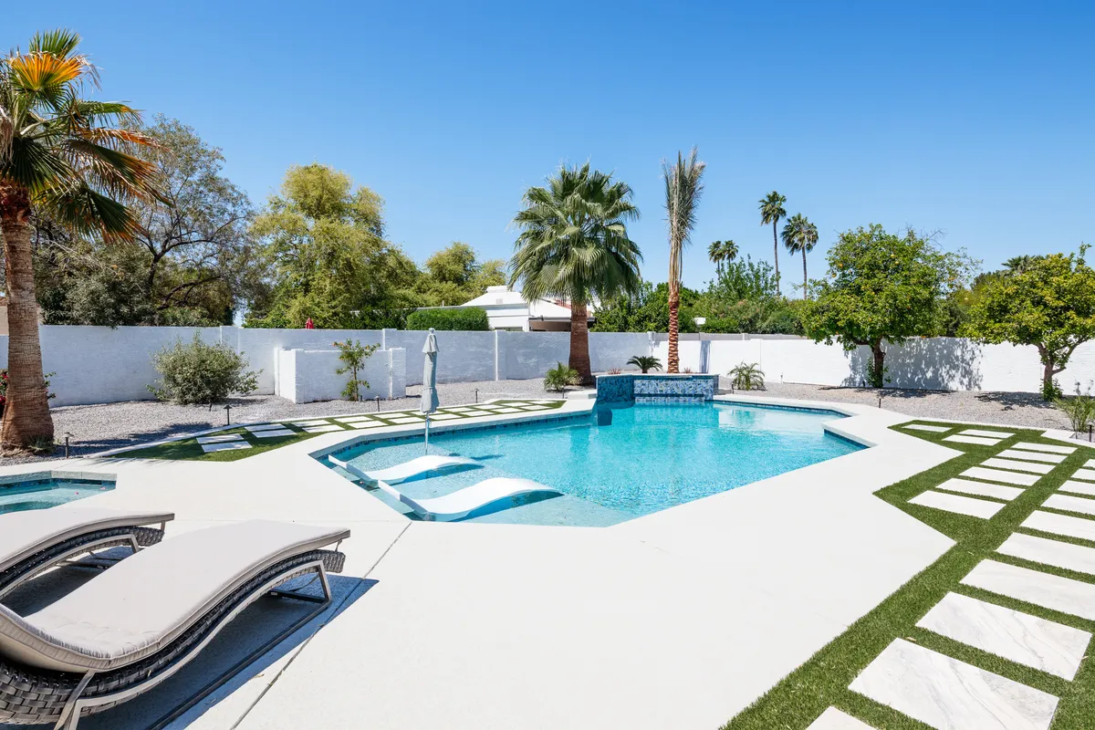 An exterior view of a luxurious private pool surrounded by lounge chairs, palm trees, and a stone pathway. The area exudes tranquility, exclusivity, and a resort-like ambiance, perfect for evening relaxation with friends or couples.