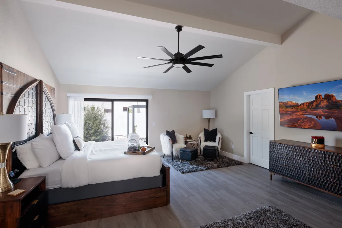 A spacious bedroom with a comfortable bed, a window view showcasing the outdoors, a wall-mounted television, and a cozy seating area. The decor is calming, with plush bedding and neutral tones creating an inviting retreat.