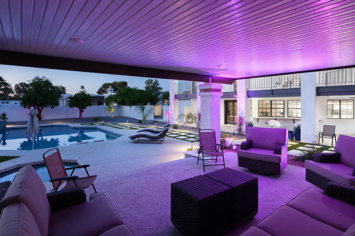 A beautifully landscaped pool area illuminated in the evening, with comfortable lounge seating and accent lighting that creates a cozy, sophisticated atmosphere. The scene suggests possibilities for stargazing, socializing, or hosting an evening barbecue by the water.