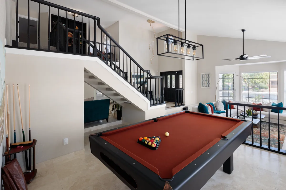 A vibrant game room centered around a sleek pool table, with a stylish staircase and a casual seating area nearby. The space is designed for socializing, friendly competition, and easy movement between activities.