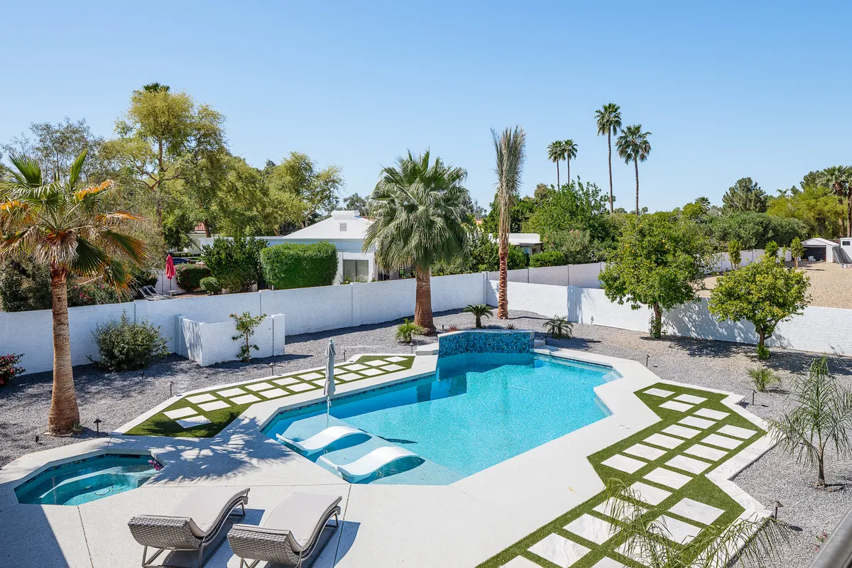 A spacious outdoor area featuring a sparkling swimming pool surrounded by lounge chairs, tall palm trees, and a lush garden. The pool is set up for both swimming and relaxing, with plenty of space for sunbathing and outdoor dining. The vibrant greenery and blue water create an inviting, resort-like atmosphere.